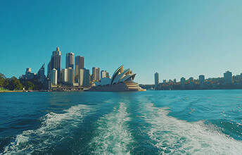 View of the Sydney Opera House and Sydney skyline from the water on a clear day with a wake trailing behind the boat, Australia.