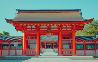 Front view of the vibrant red entrance gate (Torii) of Fushimi Inari Shrine in Kyoto, Japan, on a clear day.