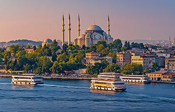 View of Istanbul, Turkey, with the Suleymaniye Mosque in the background and ferries crossing the Bosphorus River at sunset.