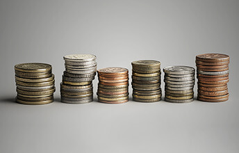 Stacks of various coins in different metals and sizes arranged in a row against a neutral background.