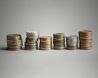 Stacks of various coins in different metals and sizes arranged in a row against a neutral background.